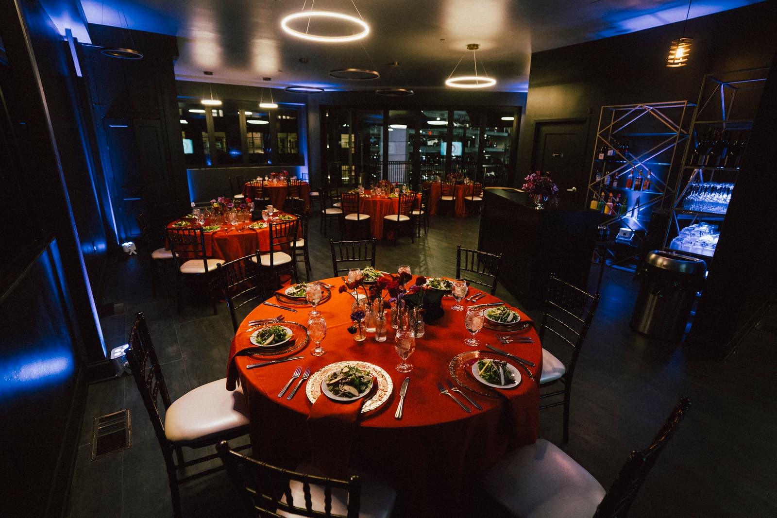 Evening dinner reception with orange-draped round tables and halo chandeliers