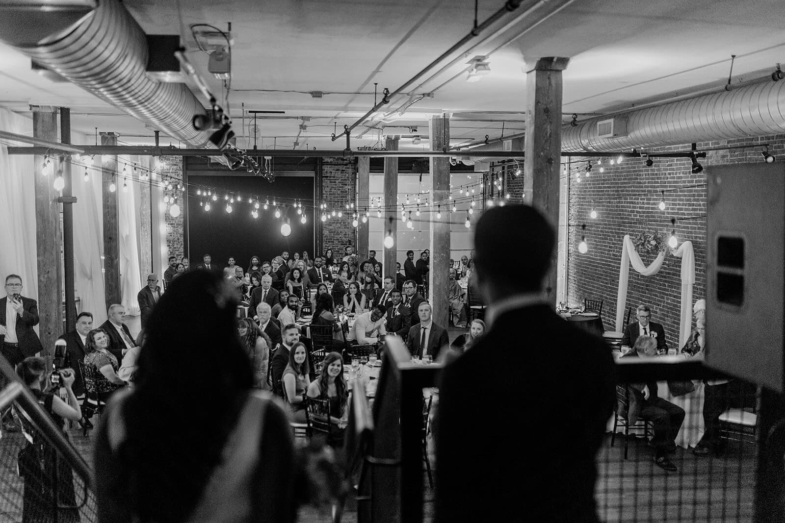 Bride and groom addressing dinner party in black and white