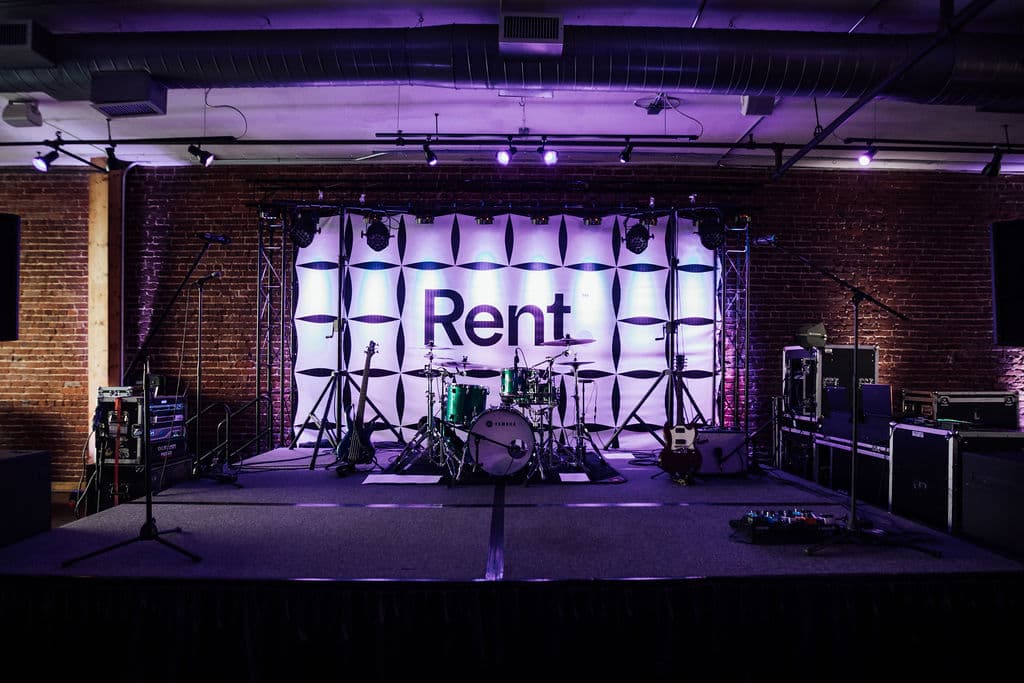 Purple-lit stage with drum kit and branded band backdrop