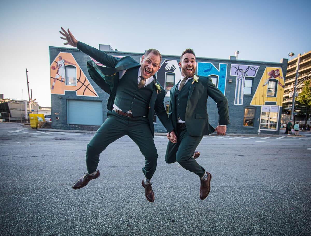 Two men in wedding attire jumping excitedly